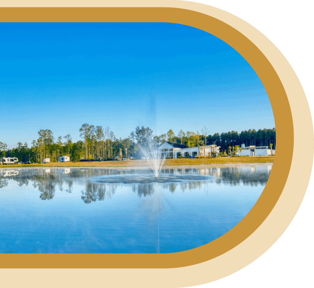 A water fountain sprays in the center of a calm pond, reflecting nearby trees and buildings under a clear blue sky, framed by rounded gold borders.